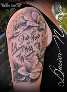 Florales Tattoo mit Spruch ‚Sei wild und wunderbar‘ am Oberarm